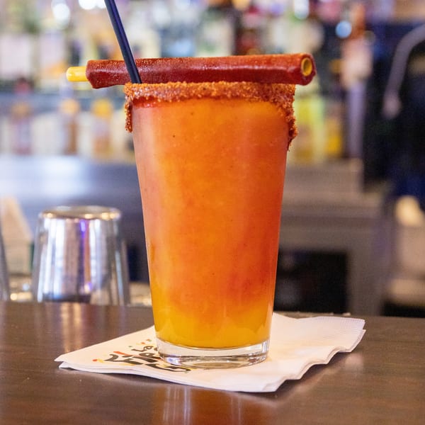 A vibrant orange and yellow frozen drink with a chili-rimmed glass and a tamarind candy straw.