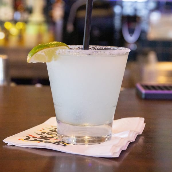 A frosty margarita with a salted rim and lime wedge, on a napkin at a bar.