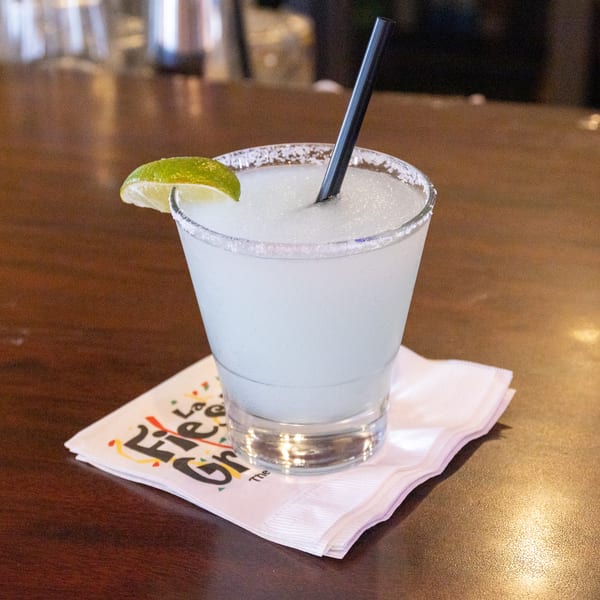Frozen margarita with a lime wedge and salted rim on a branded napkin at a bar.