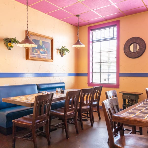 Restaurant interior with blue booths, tiled tables, wooden chairs, and peach walls with pink trim.