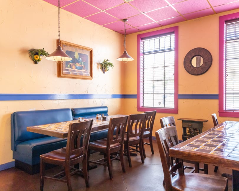 Restaurant interior with blue booths, tiled tables, wooden chairs, and peach walls with pink trim.