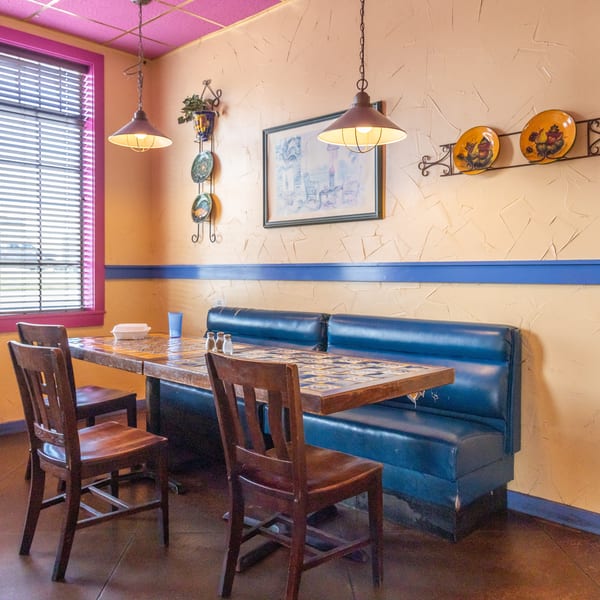 A vibrant restaurant interior with a blue booth, wooden chairs, and a tiled table under hanging lights.
