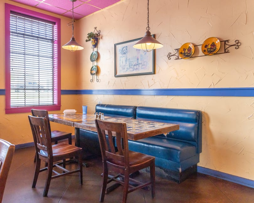 A vibrant restaurant interior with a blue booth, wooden chairs, and a tiled table under hanging lights.