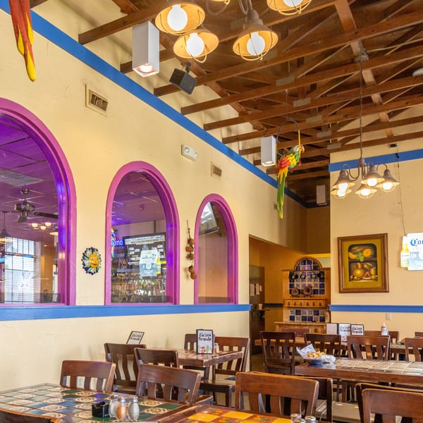 Vibrant Mexican restaurant interior with colorful decor, tiled tables, wooden chairs, and arched windows.
