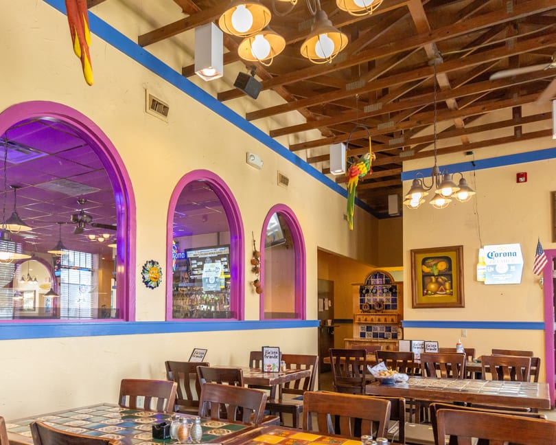 Vibrant Mexican restaurant interior with colorful decor, tiled tables, wooden chairs, and arched windows.