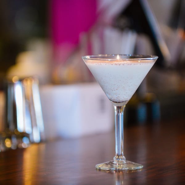 A creamy martini with a sprinkle of spices sits on a dark wooden bar.