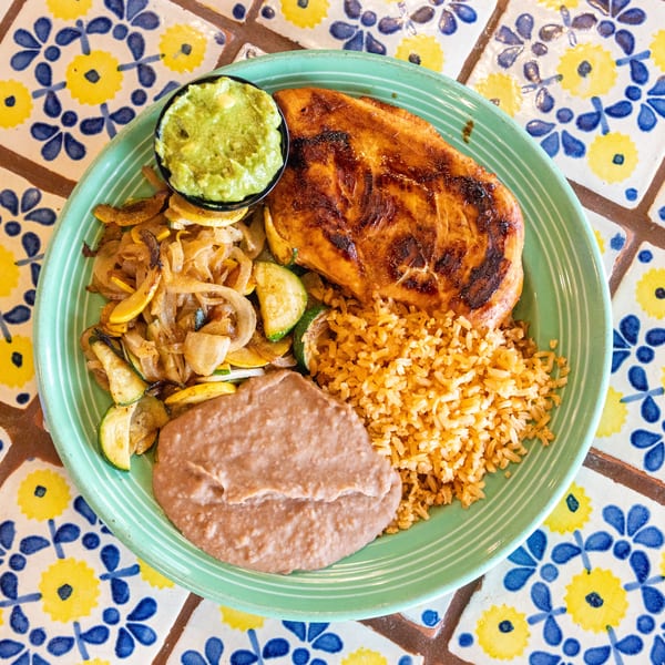Grilled chicken, rice, refried beans, sauteed vegetables, and guacamole on a green plate.