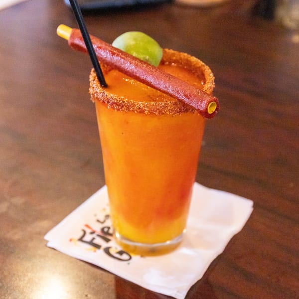 Orange drink with a chili-lime rim, a lime wedge, and a tamarind candy straw.
