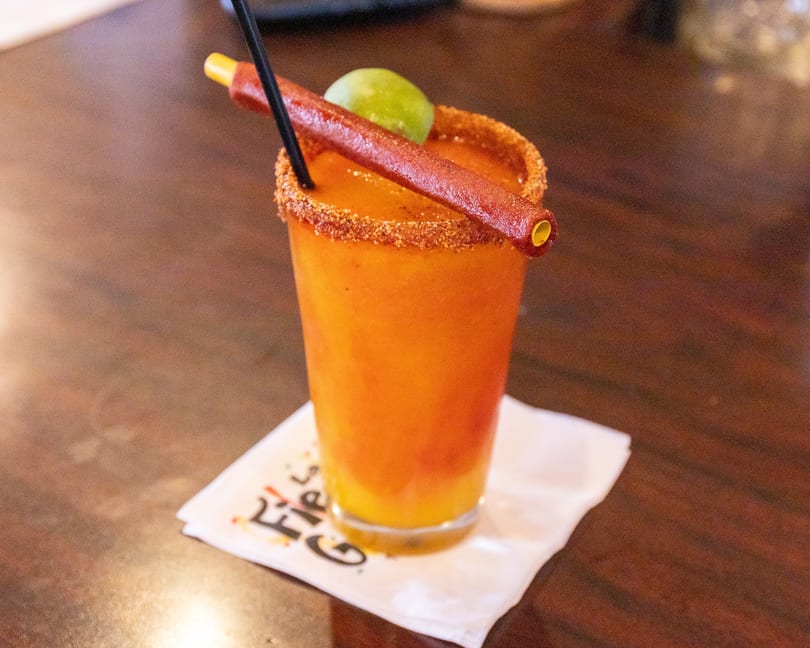 Orange drink with a chili-lime rim, a lime wedge, and a tamarind candy straw.