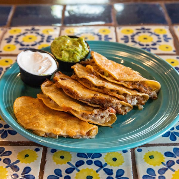 A plate of golden-brown quesadillas with melted cheese and meat, served with guacamole and sour cream.