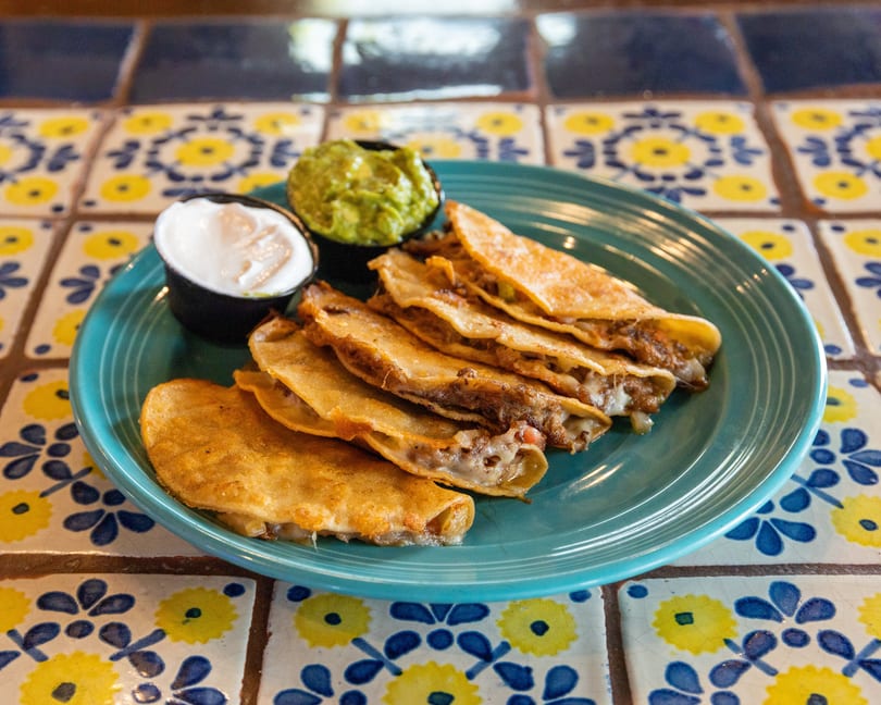 A plate of golden-brown quesadillas with melted cheese and meat, served with guacamole and sour cream.