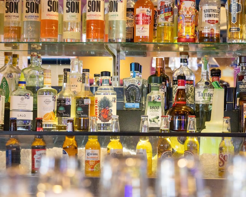 A well-stocked bar shelf with various liquor bottles, including vodkas, tequilas, and liqueurs.