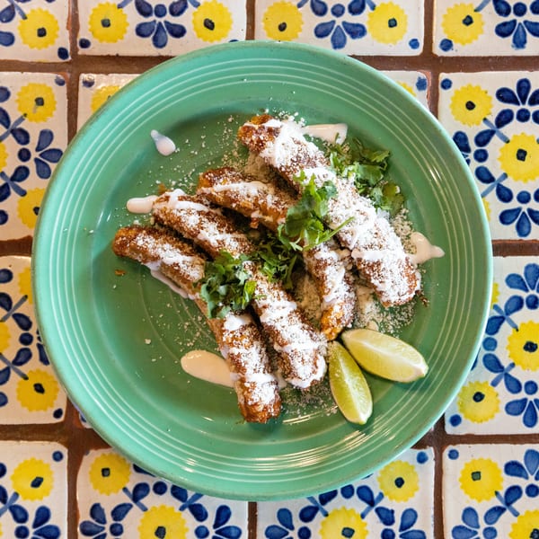 Fried plantains with white sauce, crumbled cheese, cilantro, and lime wedges on a green plate.
