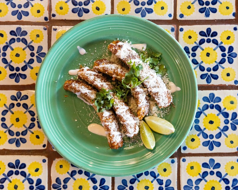 Fried plantains with white sauce, crumbled cheese, cilantro, and lime wedges on a green plate.