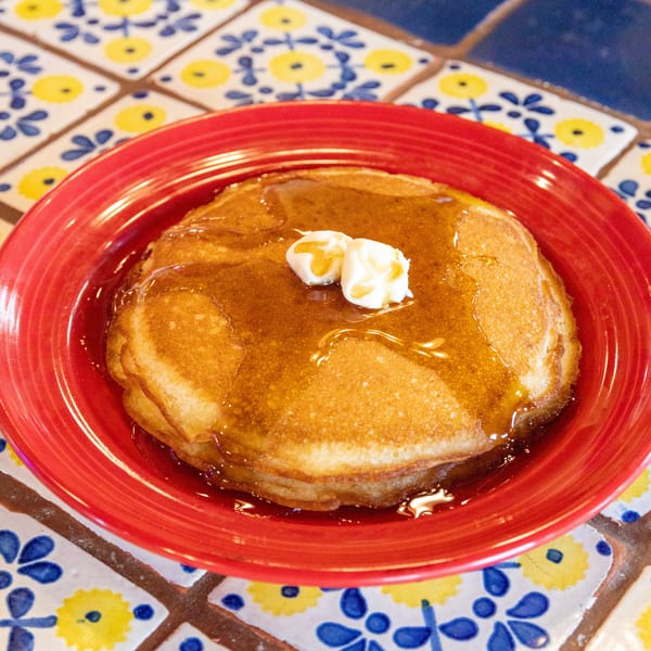 Golden pancakes with butter and syrup on a red plate, on a colorful tiled table.