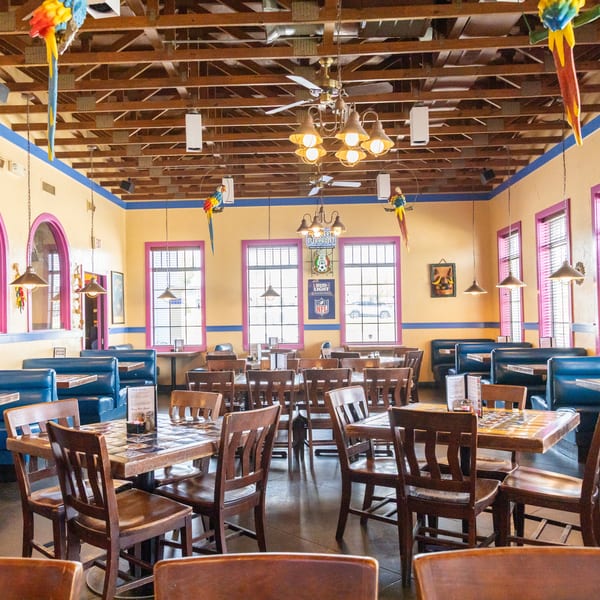 Colorful Mexican restaurant interior with blue booths, wooden tables, exposed beams, and decorative parrots.