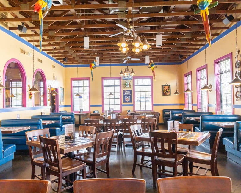 Colorful Mexican restaurant interior with blue booths, wooden tables, exposed beams, and decorative parrots.