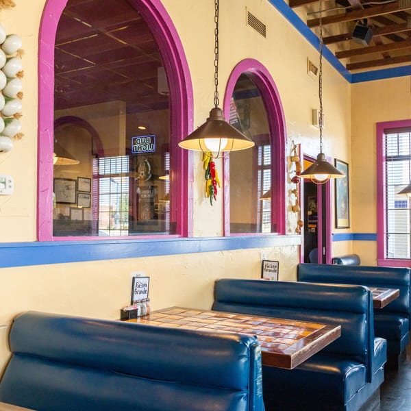 Interior of a vibrant Mexican restaurant with blue booths, tiled tables, and arched windows with pink trim.