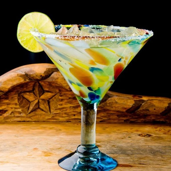Colorful margarita in a speckled glass with a lime wedge and salted rim on a wooden surface.