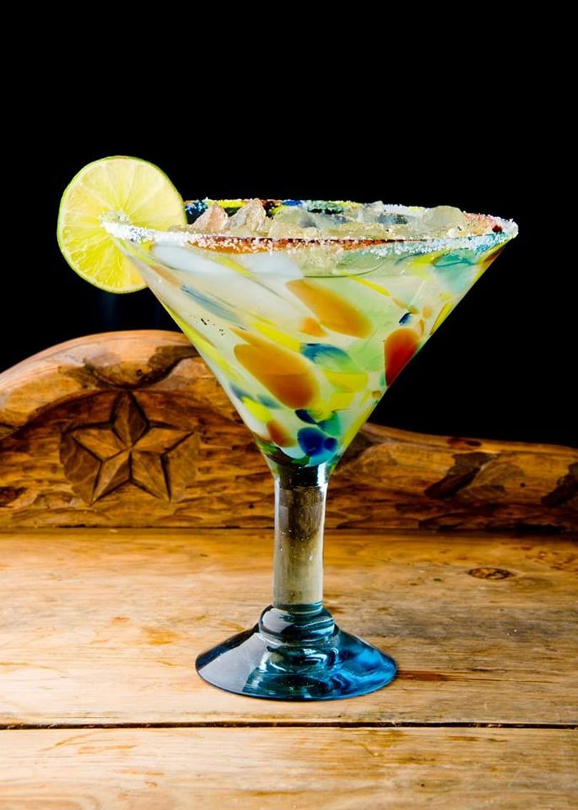Colorful margarita in a speckled glass with a lime wedge and salted rim on a wooden surface.